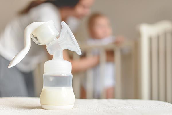Milchpumpe, im Hintergrund Mutter mit Baby