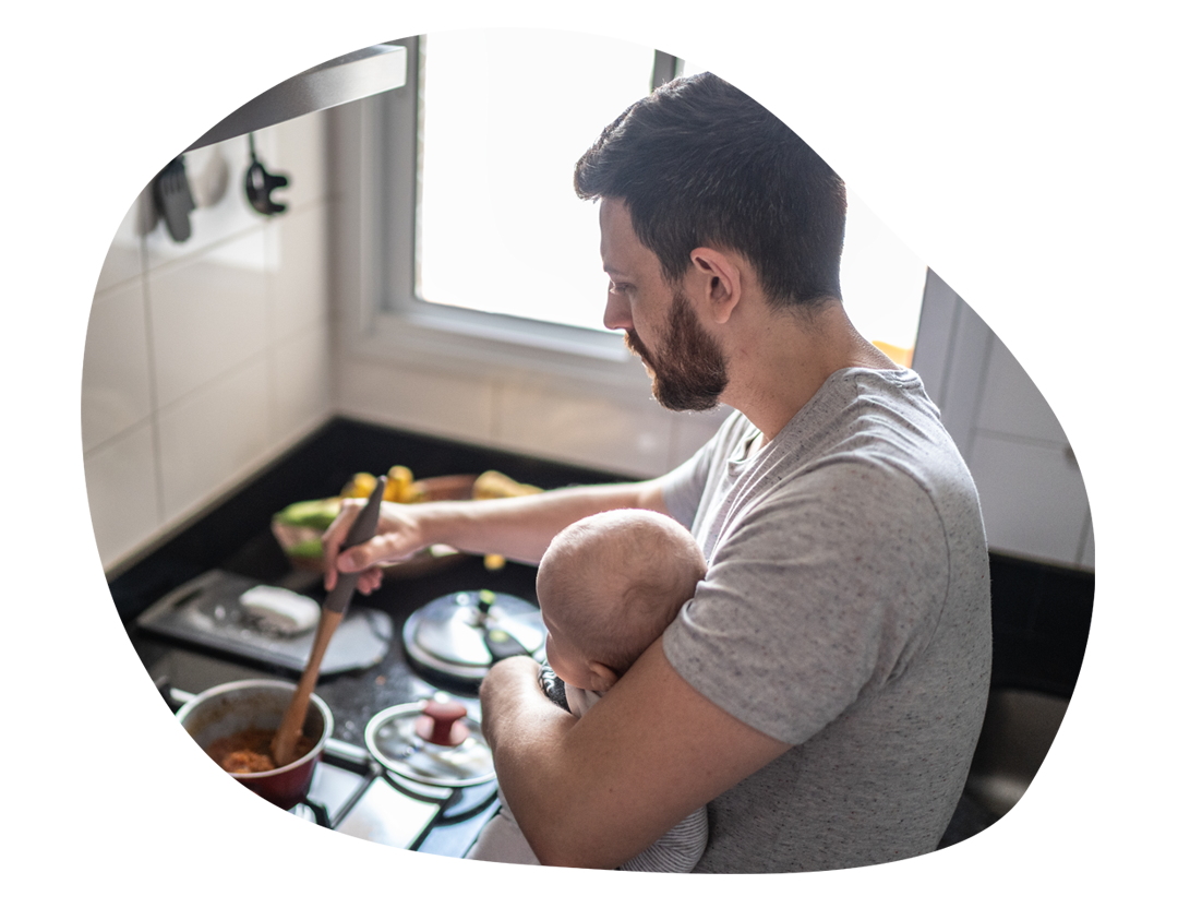 Mann hält ein Baby am Arm während er kocht